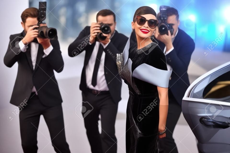 Piękna kobieta ubrana w stylu retro jako słynna aktorka filmowa przybywająca na ceremonię wręczenia nagród z fotoreporterami robiącymi jej zdjęcia