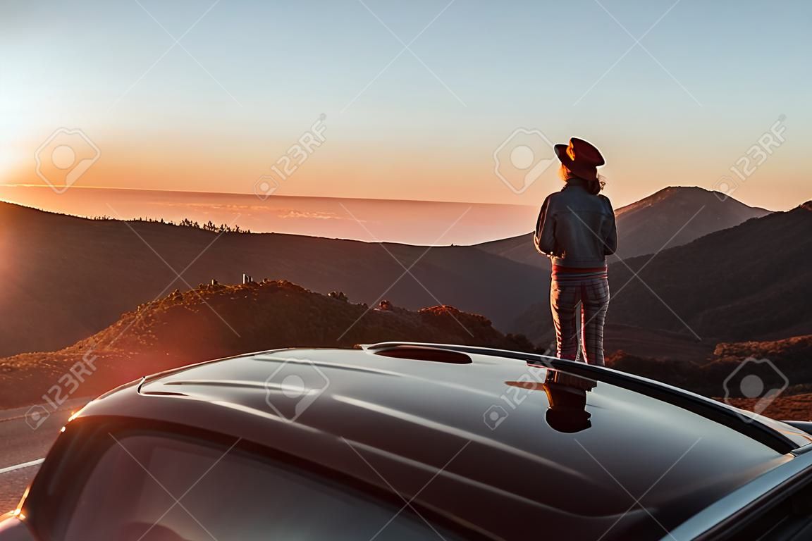 Vue paysage au bord de la route au-dessus des nuages avec une femme profitant d'un magnifique coucher de soleil tout en voyageant sur la voiture de sport décapotable