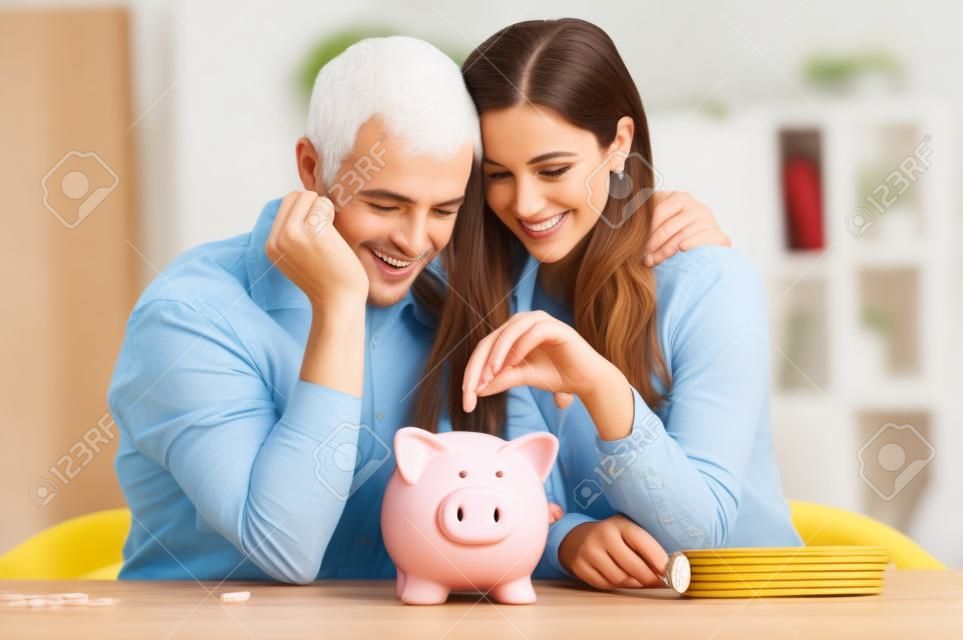 Retrato de pareja feliz que inserta la moneda en Piggybank