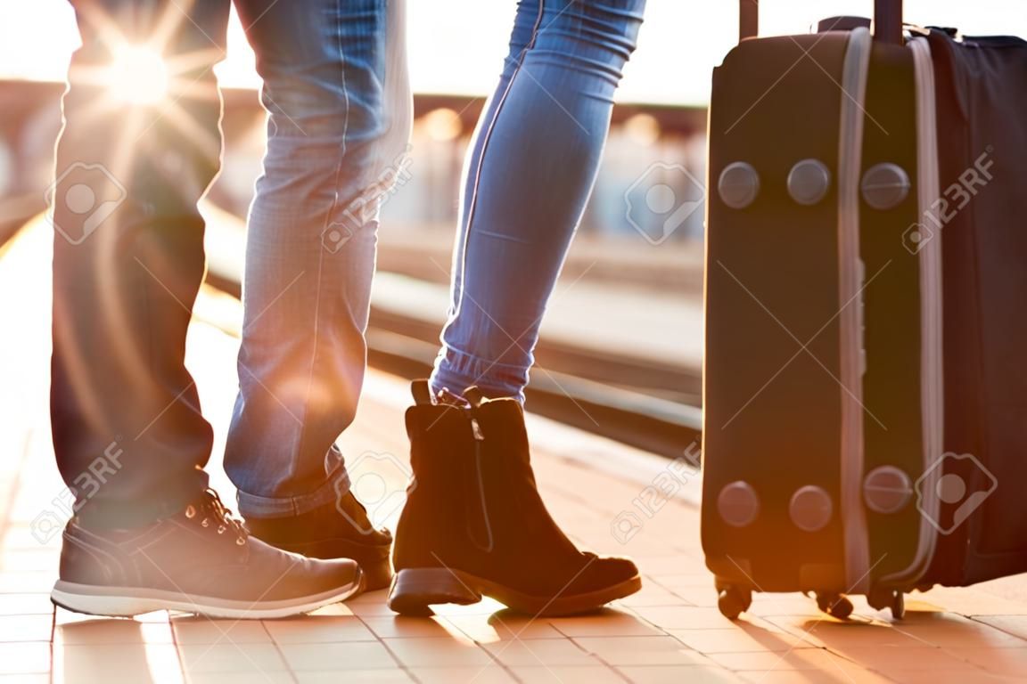 Closeup shot of woman feet standing on tiptoe while embracing her man at railway platform for a farewell before train departure. A travelling luggage is on the foreground. Beautiful warm sunset light and flare are coming from the background.