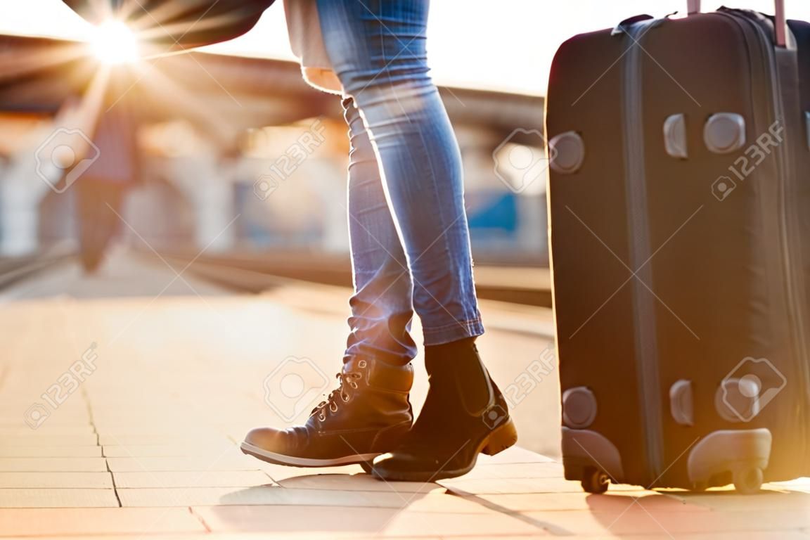 Closeup shot of woman feet standing on tiptoe while embracing her man at railway platform for a farewell before train departure. A travelling luggage is on the foreground. Beautiful warm sunset light and flare are coming from the background.