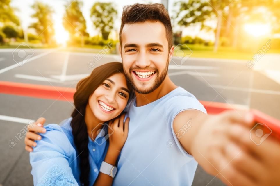 Крупным планом выстрел из молодой пары принять selfie на открытом воздухе. Молодой человек, принимая фотографии с его подругой. Happpy улыбается пара, принимая selfie в летний день.