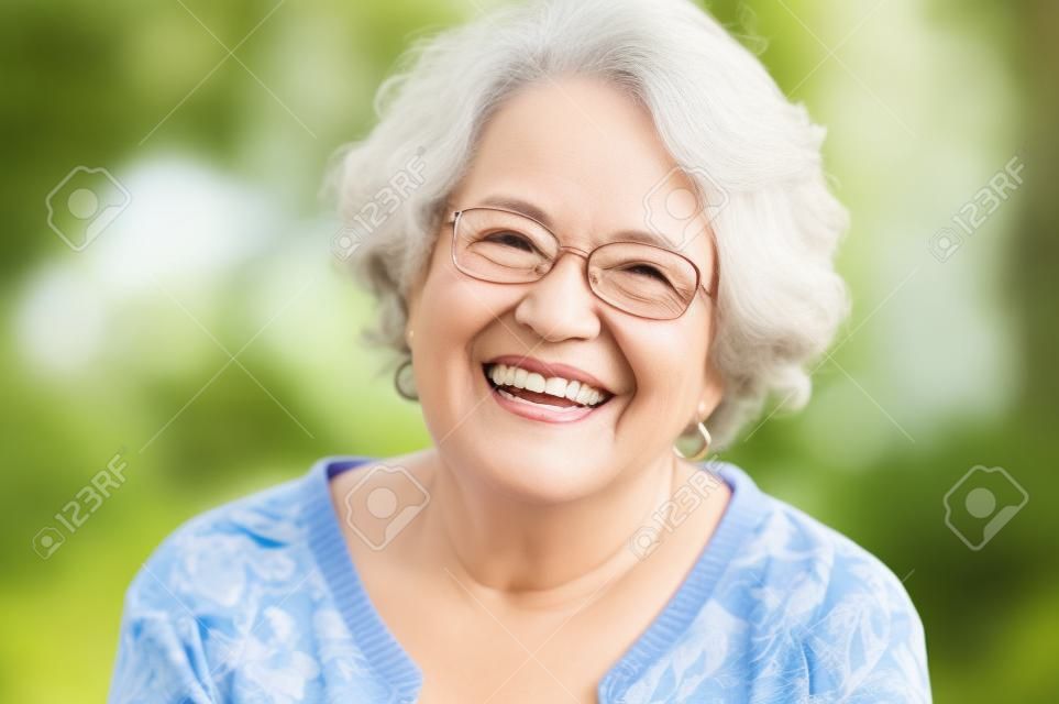Ritratto di donna senior sorridendo e guardando fotocamera. Occhiali d'uso della donna matura allegra nel parco. Donna anziana felice con sorridere dei capelli grigi. Donna pensionata spensierata e positiva.