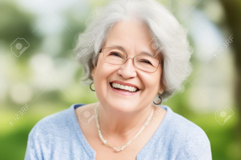 Portrait der älteren Frau lächelnd und auf Kamera. Fröhlich reife Frau Brille im Park tragen. Glückliche alte Frau mit grauen Haaren lächelnd. Sorglos und positive pensionierte Frau.