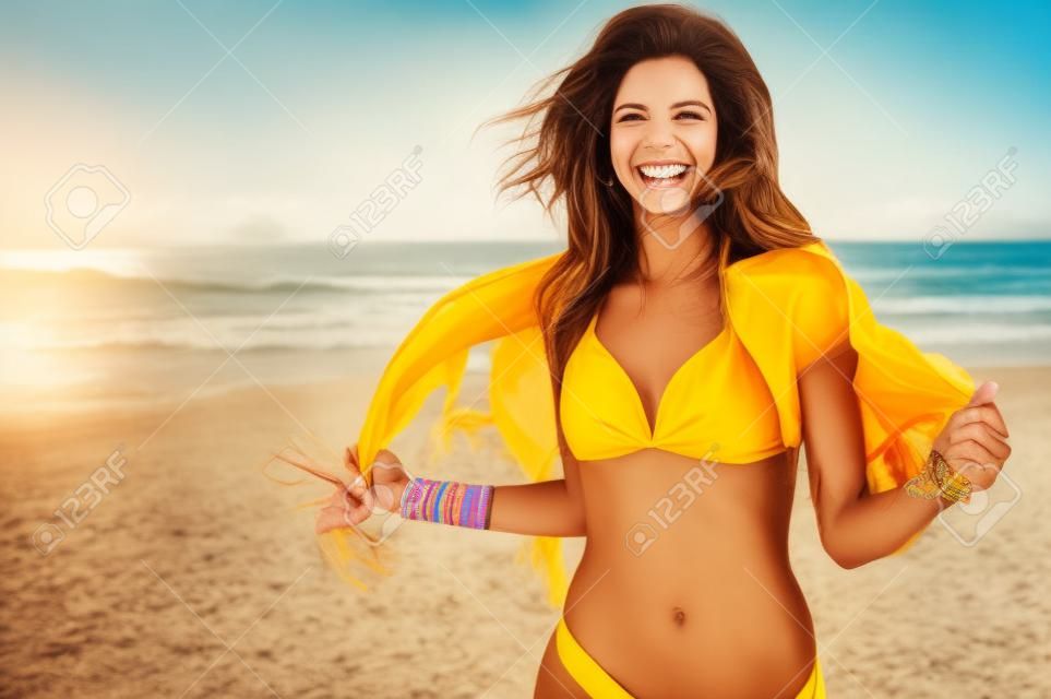 Heureuse femme souriante et s'amuser à la plage. Portrait d'été de belle jeune fille courir sur la plage avec un foulard jaune. Fille latine en riant et en regardant la caméra avec joie.