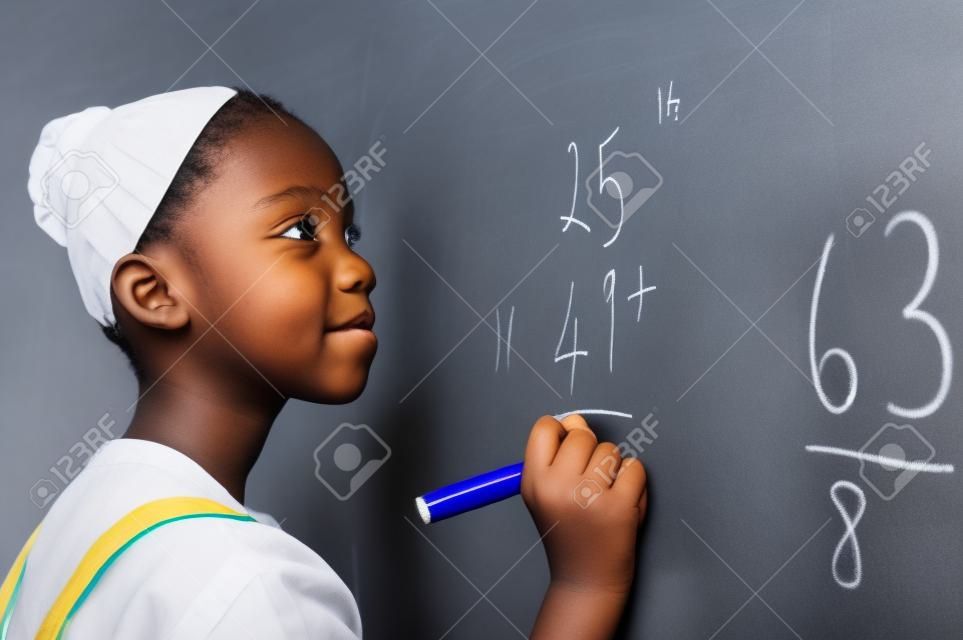 Portret afrykańskiej dziewczyny, pisząc rozwiązanie sum na tablicy w szkole. Czarna uczennica rozwiązuje sumę dodawania na białej tablicy za pomocą markera. Dziecko w wieku szkolnym myśli podczas rozwiązywania problemu matematycznego.