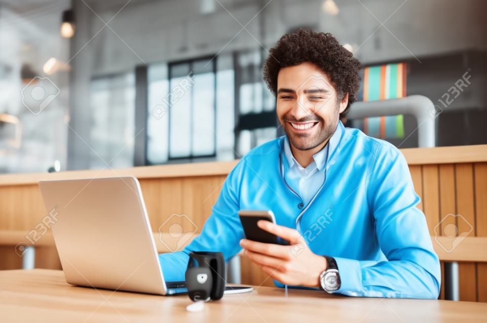Portrait d'homme d'affaires utilisant un smartphone avec écouteurs et ordinateur portable pour une conférence d'affaires. Joyeux homme d'affaires souriant assis au restaurant en écoutant de la musique. Heureux homme bénéficiant d'une connexion Internet sans fil gratuite au café.