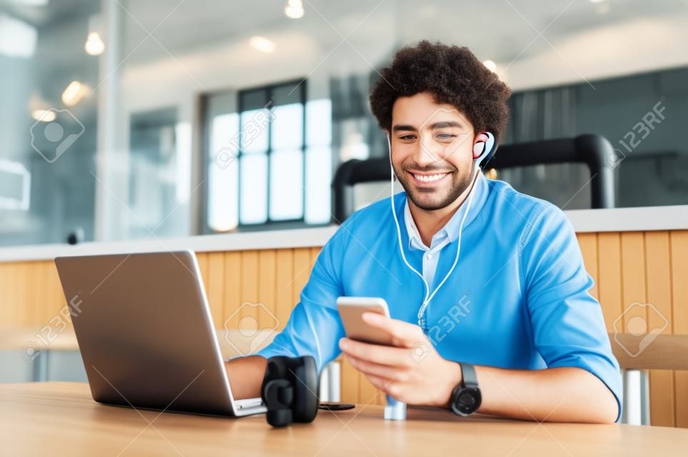 Portrait d'homme d'affaires utilisant un smartphone avec écouteurs et ordinateur portable pour une conférence d'affaires. Joyeux homme d'affaires souriant assis au restaurant en écoutant de la musique. Heureux homme bénéficiant d'une connexion Internet sans fil gratuite au café.