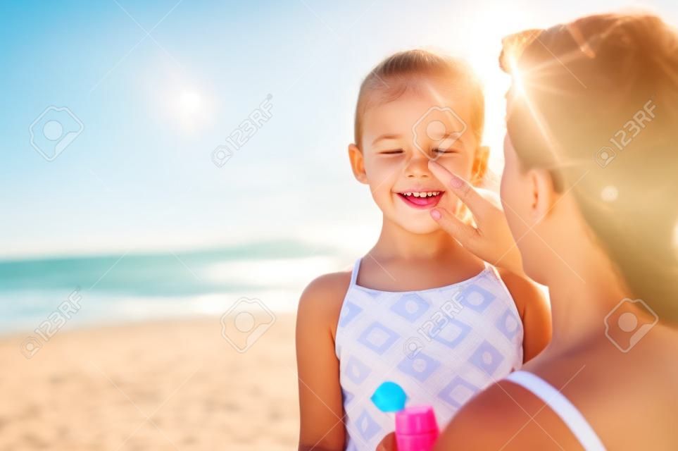 Jeune mère appliquant un écran solaire protecteur sur le nez de sa fille à la plage. Main de femme mettant de la crème solaire sur le visage de l'enfant. Jolie petite fille avec crème solaire au bord de la mer avec espace de copie.
