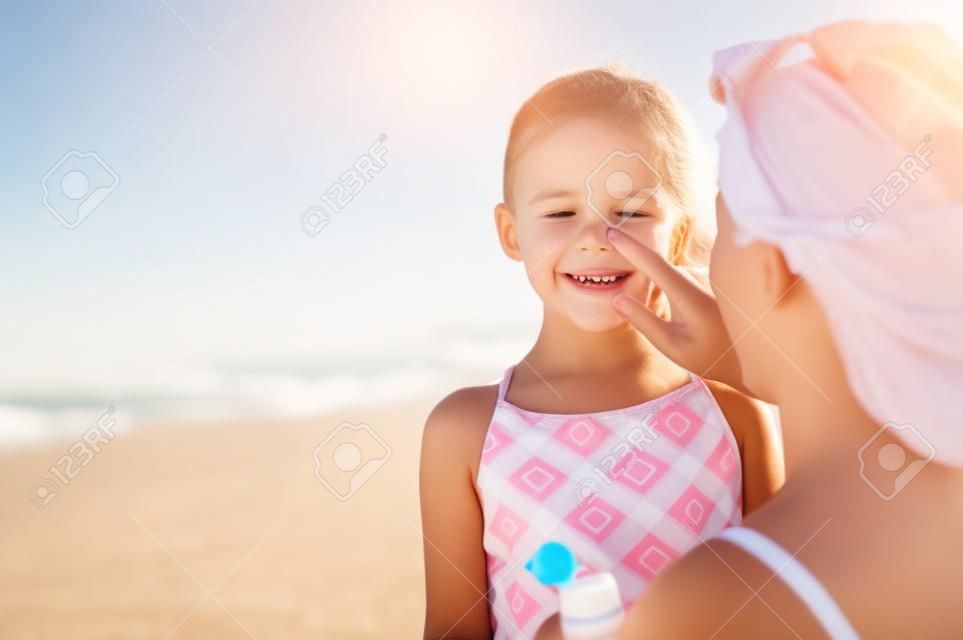 해변에서 딸 코에 보호용 자외선 차단제를 바르는 젊은 어머니. 여자 손 아이 얼굴에 썬 로션을 퍼 팅입니다. 복사 공간이 있는 해변에서 자외선 차단제를 바르는 귀여운 소녀.
