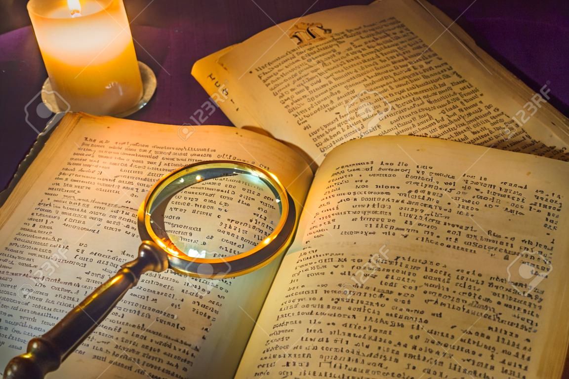 An open ancient prayer books and a magnifying glass on its open pages under the light of a candle