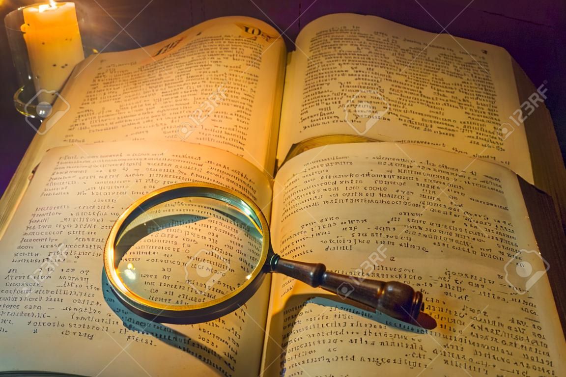 Un livre de prières ancien ouvert et une loupe sur ses pages ouvertes à la lumière d'une bougie