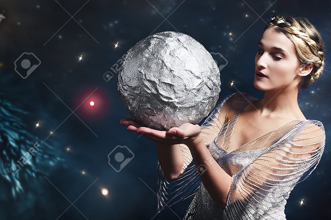 Kobieta trzyma srebrną kulę na tle rozgwieżdżonego nieba