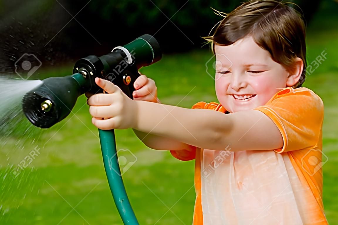Ребенок играет на улице с водой шланг летом или весной, чтобы освежиться в жаркую погоду