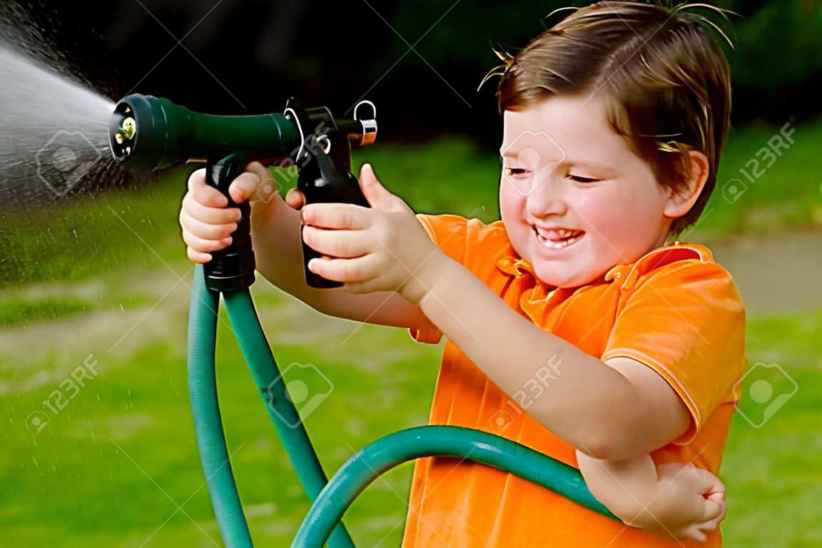 Child plays with water hose outdoors during summer or spring to cool off in hot weather