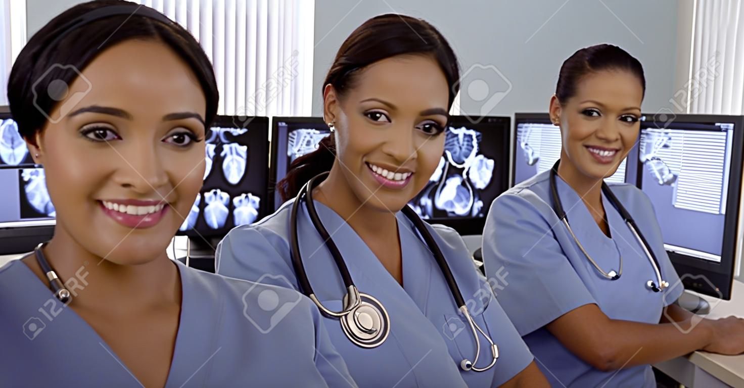 Sonreír enfermeras hispanas y afroamericanas se sientan en zona de ordenadores