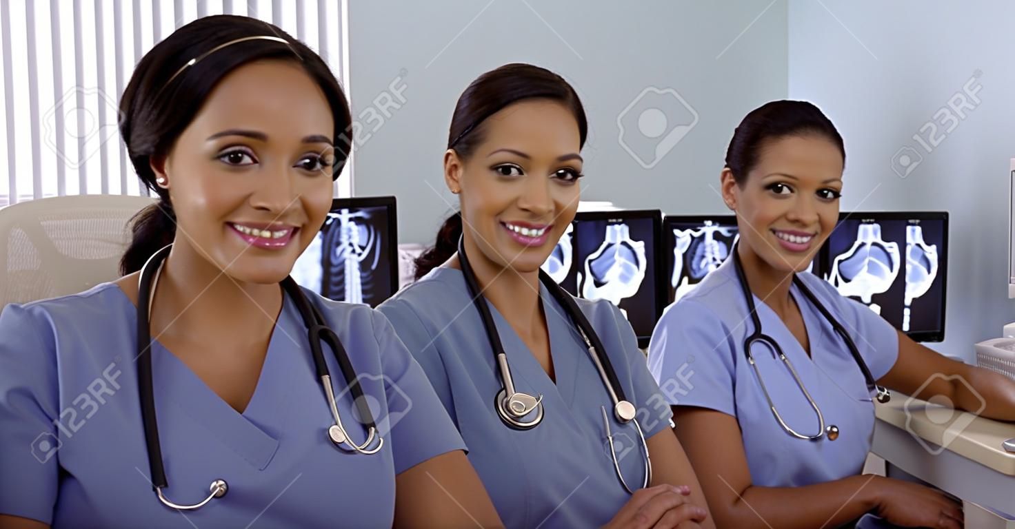 Sorridere infermieri americani ispanici e africani seduti a postazione PC