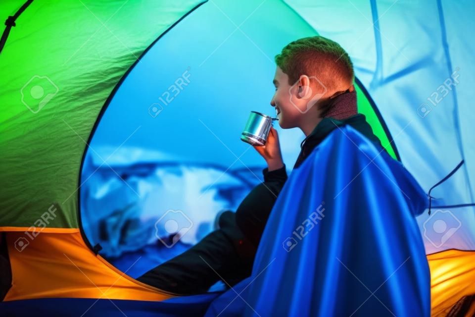 Młody turysta pije rano herbatę z kolby w namiocie