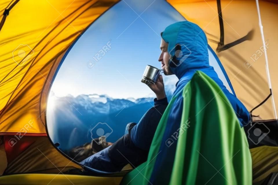 Joven excursionista bebe té del matraz en la carpa por la mañana