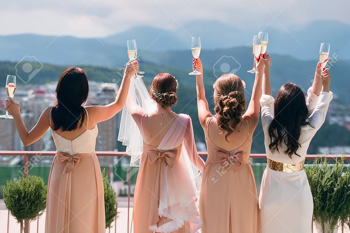 Rückansicht Braut und Freundinnen auf dem Balkon, erhobenes Glas Champagner