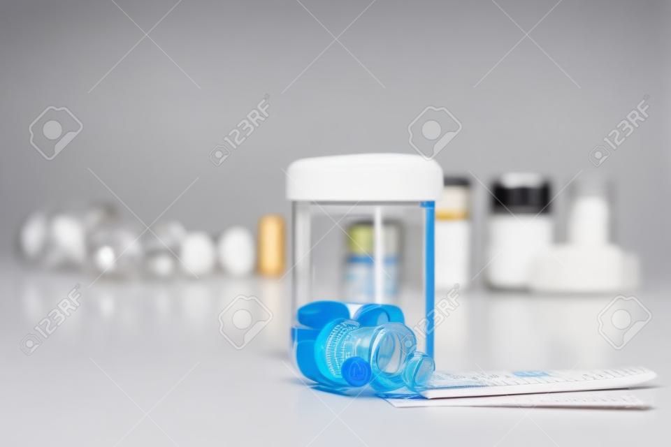 Measuring cylinder with drugs on table. Medical vials in the background.