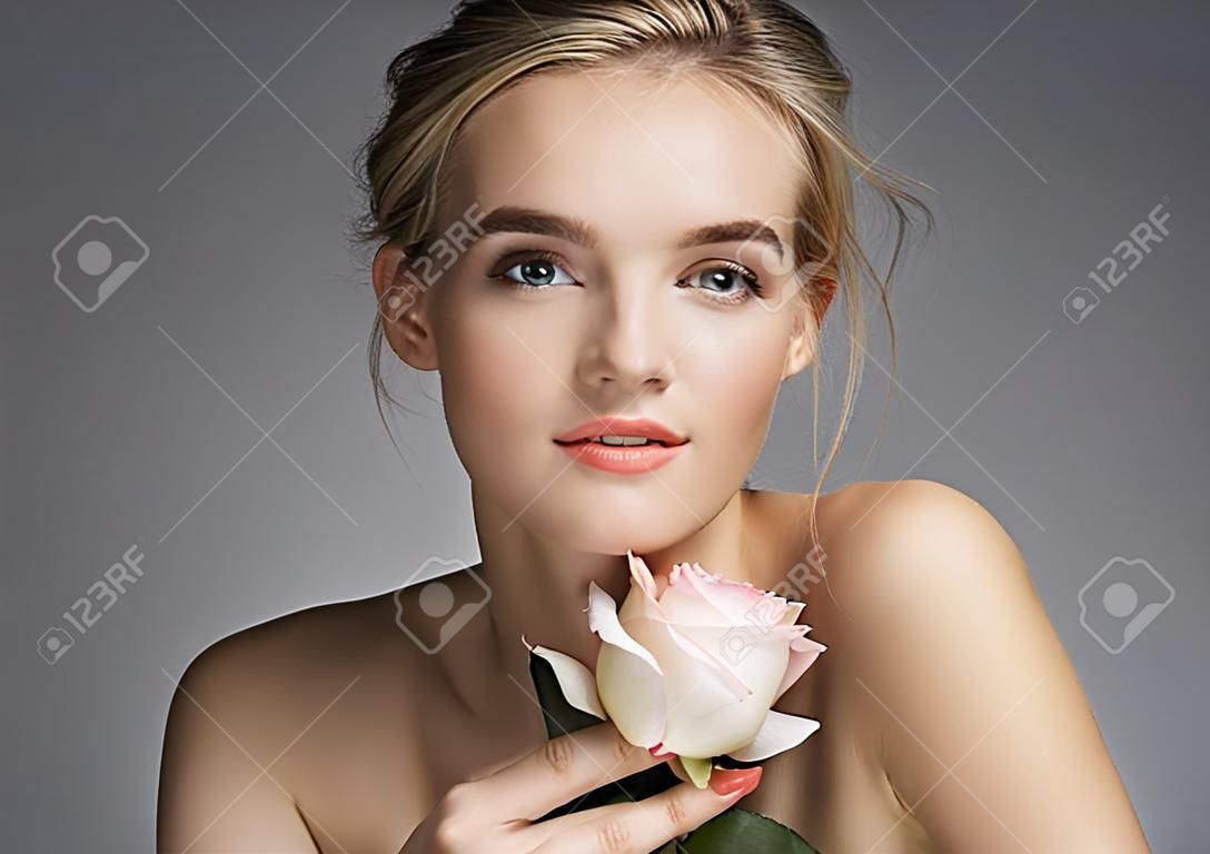 Bela jovem senhora com maquiagem natural. Foto de menina loira com rosa no fundo cinza. Conceito de cuidados com a pele