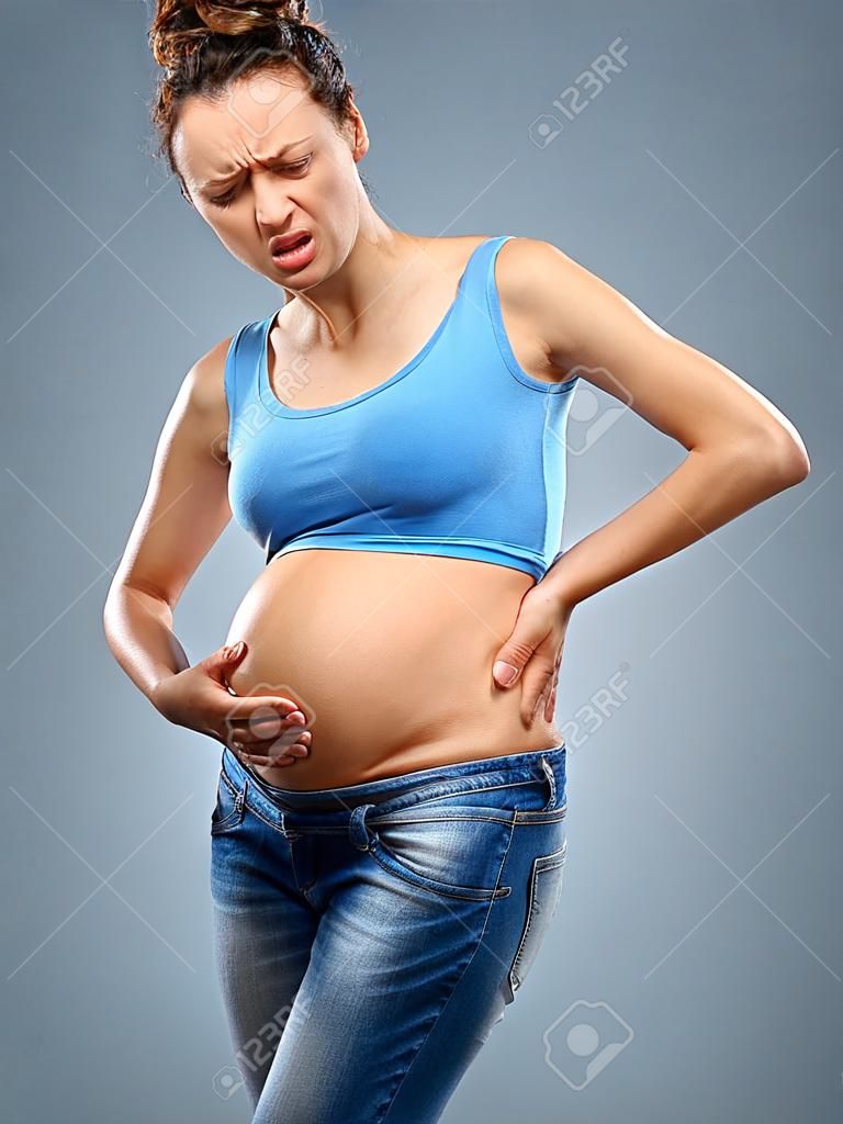 Mal di schiena. Donna incinta che tiene la sua parte bassa della schiena dolorante su sfondo grigio. Concetto medico