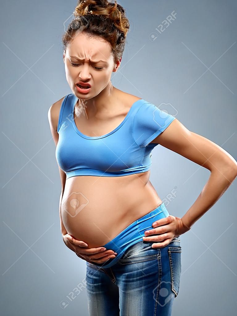 Ból pleców. Kobieta w ciąży trzymająca dolną część pleców w bólu na szarym tle. Koncepcja medyczna