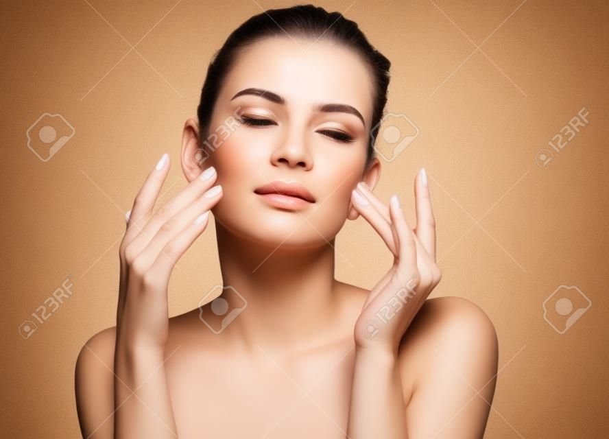 Mujer haciendo masaje facial, tocándose la cara. Foto de mujer con piel limpia y sana sobre fondo beige. Concepto de belleza y cuidado de la piel