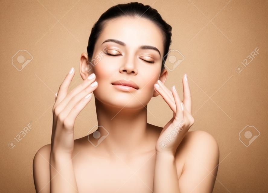 Mujer haciendo masaje facial, tocándose la cara. Foto de mujer con piel limpia y sana sobre fondo beige. Concepto de belleza y cuidado de la piel
