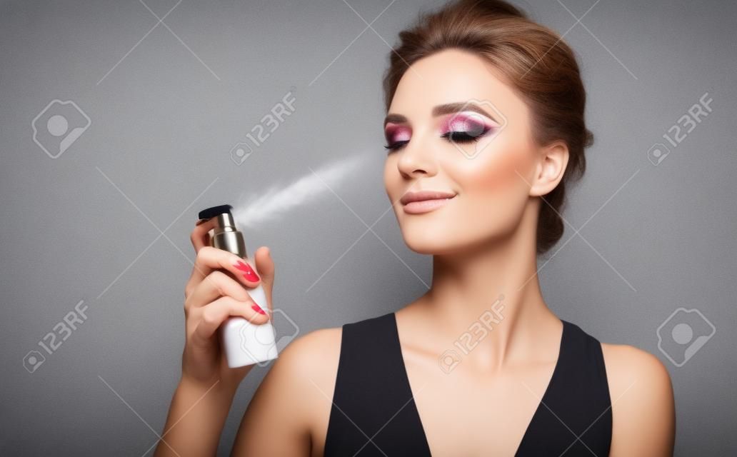 Kobieta za pomocą sprayu do wykańczania. zdjęcie kobiety z doskonałym makijażem na szarym tle. koncepcja piękna