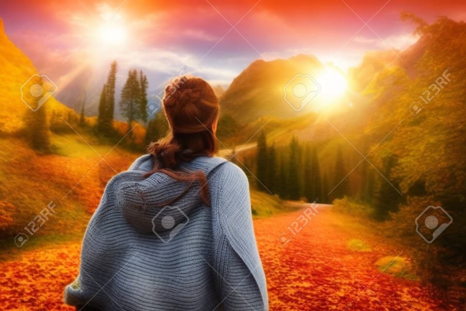 The brunette girl goes to meet the sun. Autumn walk in the mountains.