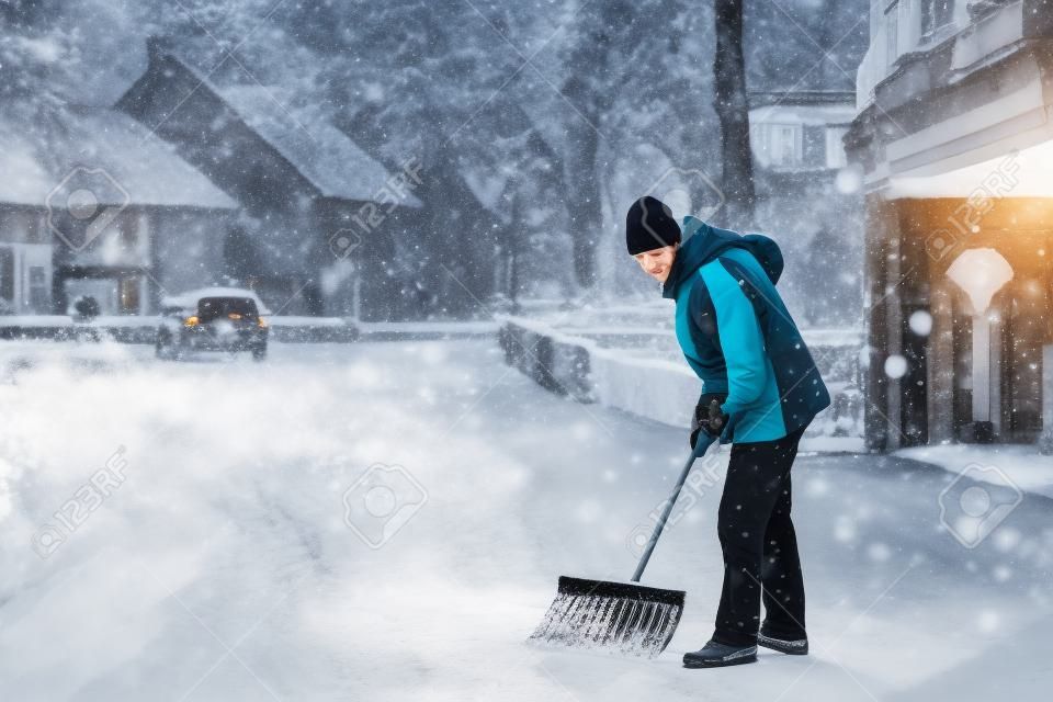 Man met sneeuwschop reinigt trottoirs in de winter. Wintertijd in Europa. Jonge man in warme winterkleding