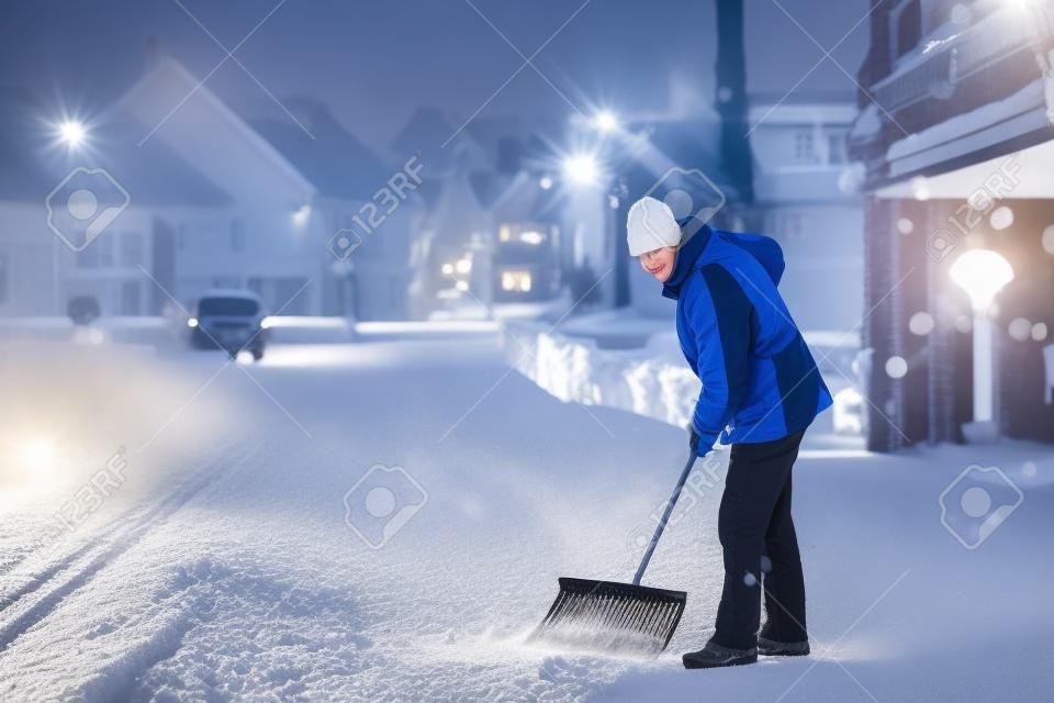 Man met sneeuwschop reinigt trottoirs in de winter. Wintertijd in Europa. Jonge man in warme winterkleding