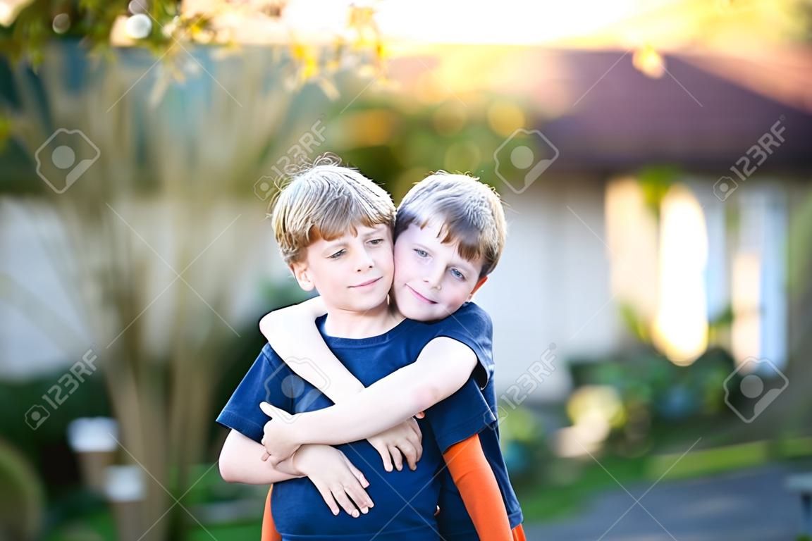 Dois pequenos meninos ativos da escola, gêmeos e irmãos abraçando no dia de verão