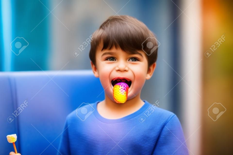 Gorgeous little school kid boy licking lollypops and showing colored blue tongue. Funny child having fun with coloring bonbon, indoors
