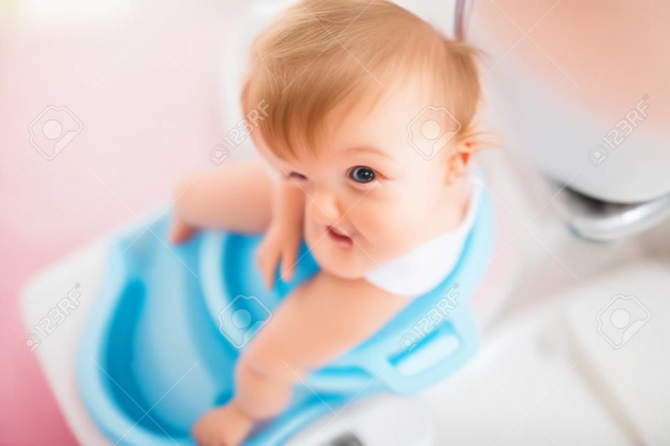 Nahaufnahme des netten kleinen Kleinkindbabykindes, das auf Toiletten-WC-Sitz sitzt. Töpfchentraining für kleine Kinder. Nicht erkennbares Gesicht des Kindes