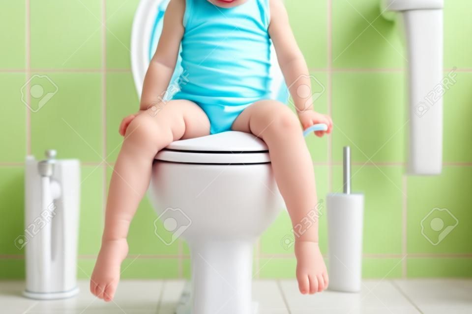 Closeup of cute little toddler baby girl child sitting on toilet wc seat. Potty training for small children. Unrecognizable face of child