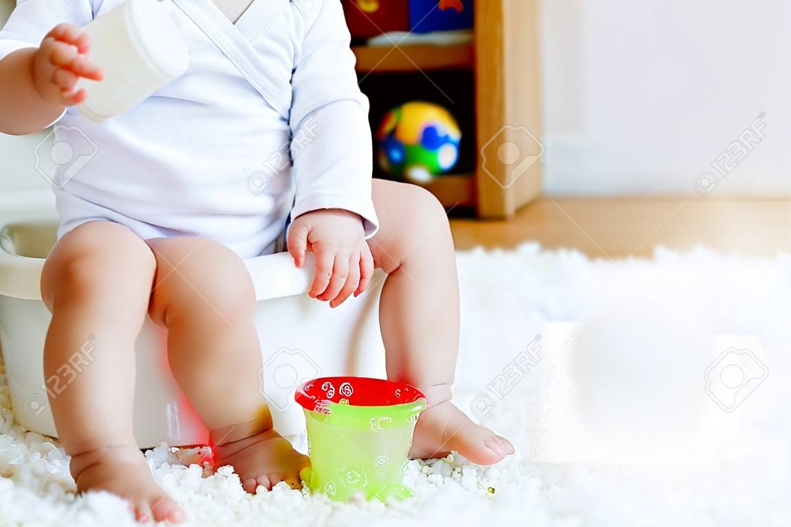 Closeup of cute little old toddler baby girl child sitting on potty. Kid playing with educational toy and Toilet training concept. Baby learning, development steps. No face, unrecognizable person.