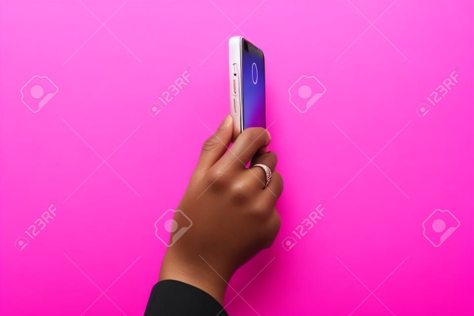 Mobile phone in female hand. Blogger or journalist during the online broadcast. Pink background. Vertical photo or video mode.