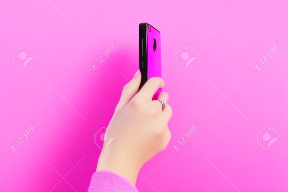 Mobile phone in female hand. Blogger or journalist during the online broadcast. Pink background. Vertical photo or video mode.