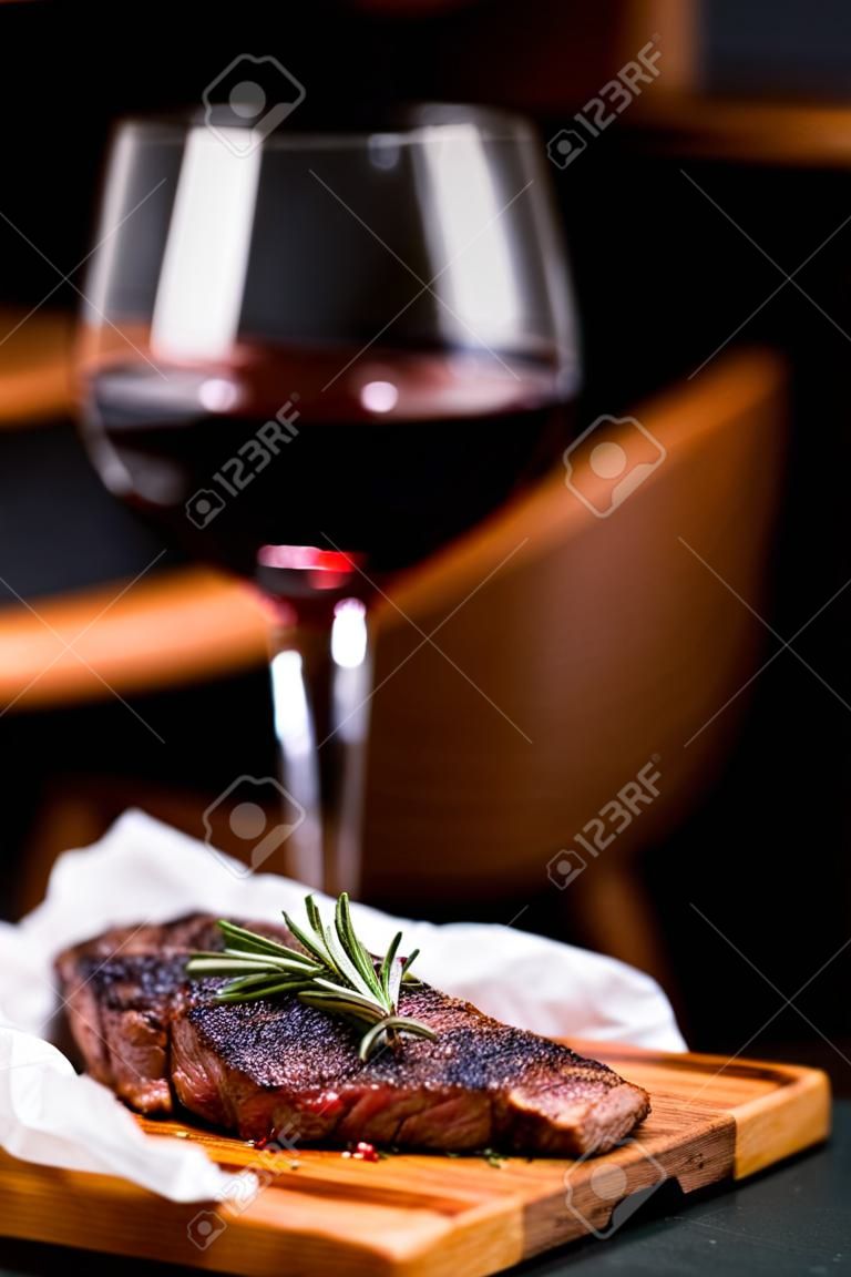 Striploin gegrilde rundvlees biefstuk geserveerd met rozemarijn, zout en pepercorns op houten plank met glas wijn.