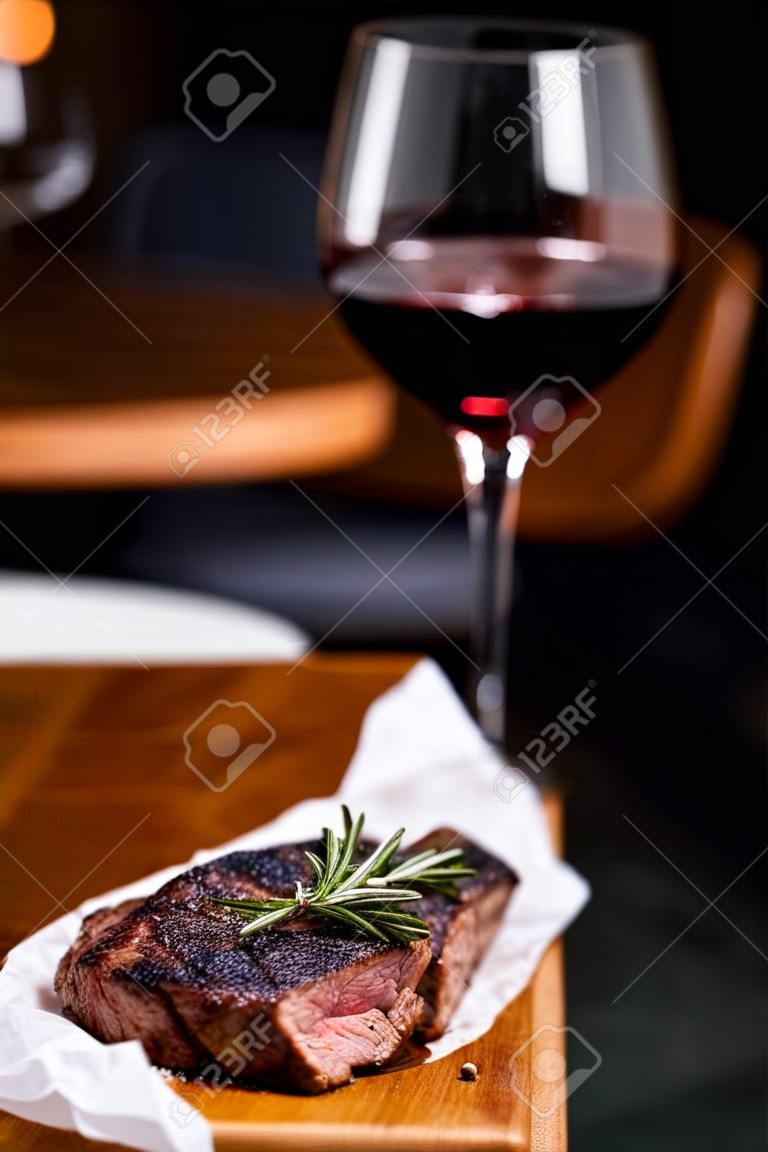 Striploin gegrilde rundvlees biefstuk geserveerd met rozemarijn, zout en pepercorns op houten plank met glas wijn.