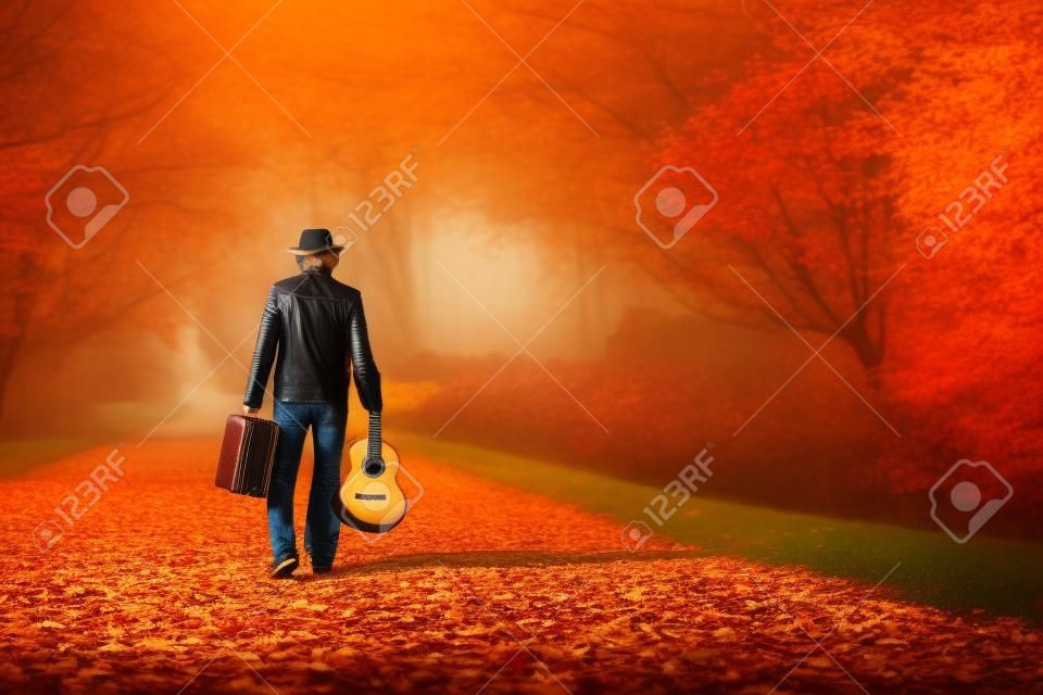 Vintage bavul ve gitar boş sonbahar yol kopya uzay arka plan üzerinde walking away retro şapka ve deri ceket Genç adam, müzisyen