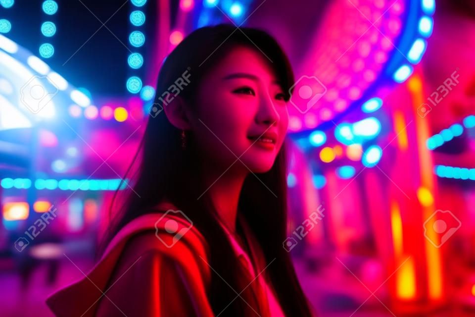 Linda mulher asiática no parque de diversões à noite com luz vermelha