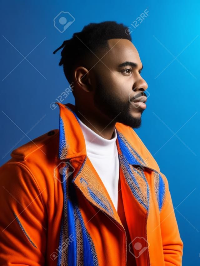 Hübscher afroamerikanischer mann in orangefarbener jacke auf blauem hintergrund