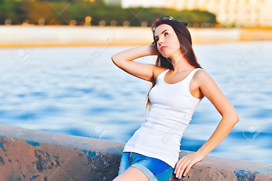 Hipster girl wearing blank white t-shirt and jeans posing against river, minimalist urban clothing style, mockup for tshirt print store