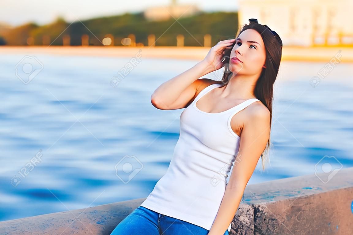 Hipster girl wearing blank white t-shirt and jeans posing against river, minimalist urban clothing style, mockup for tshirt print store