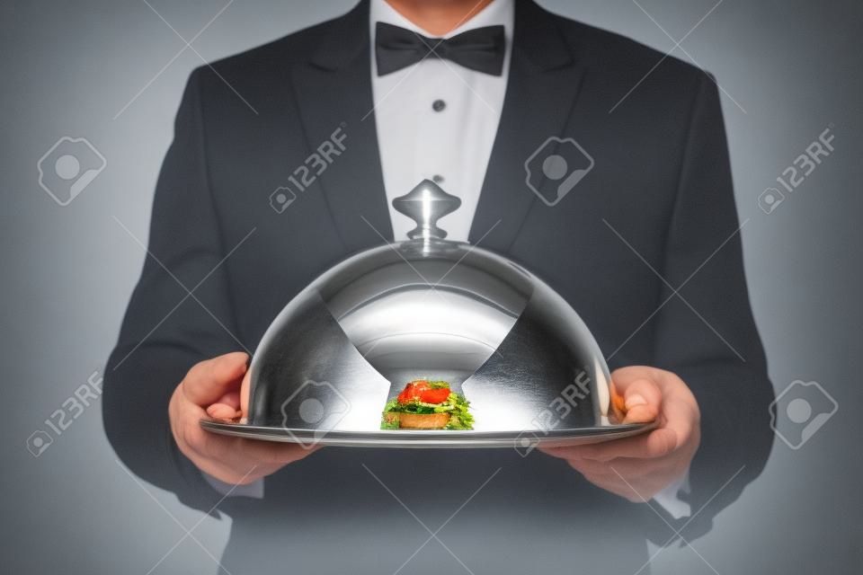 Ober serveert een maaltijd onder een zilveren cloche of koepel