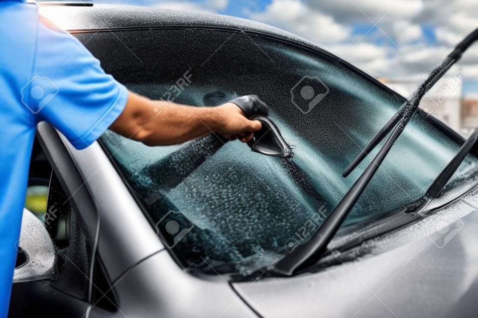 Mężczyzna myje przednią szybę samochodu